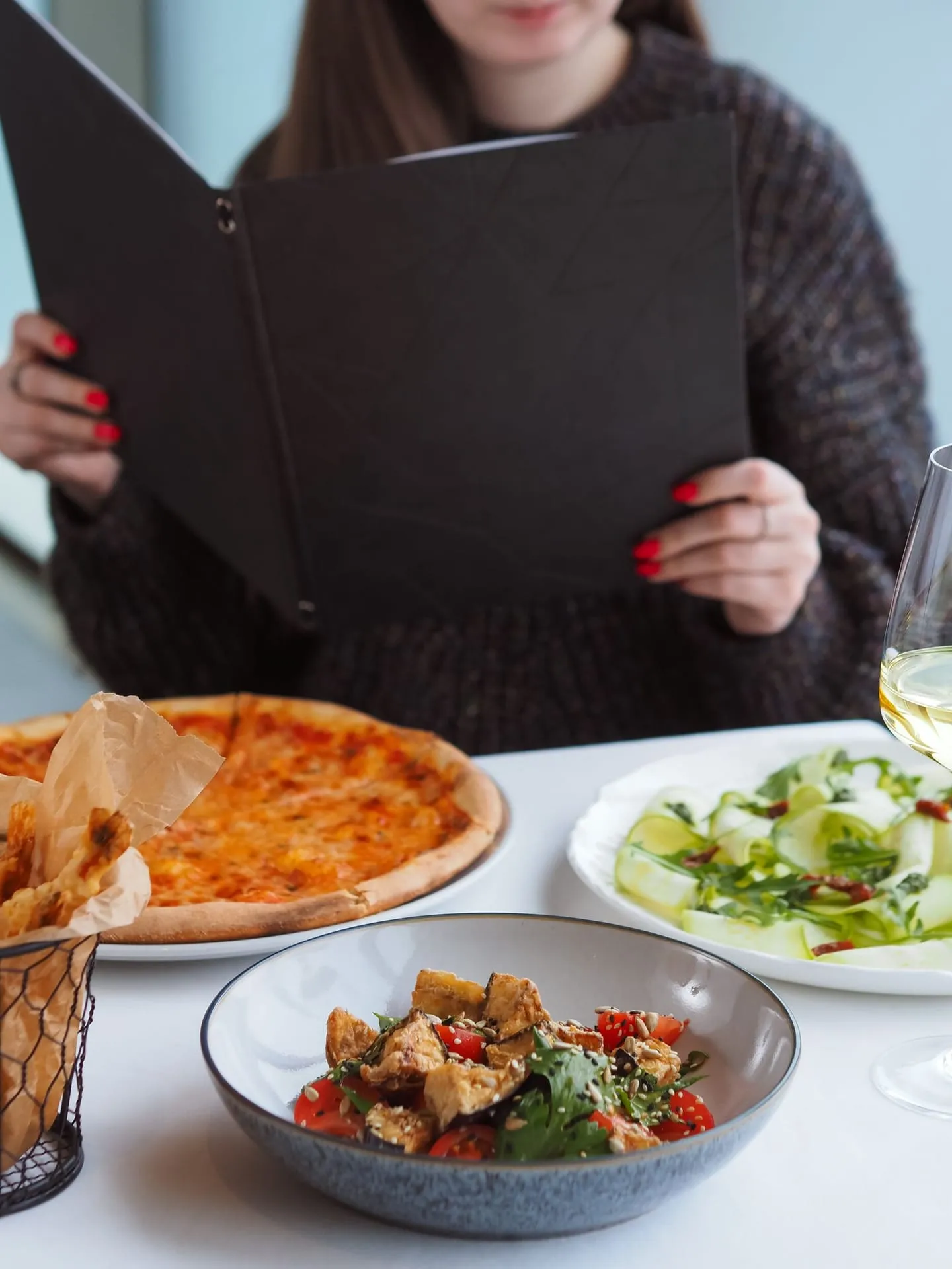 Una mujer en la mesa con pizza, ensalada y la carta