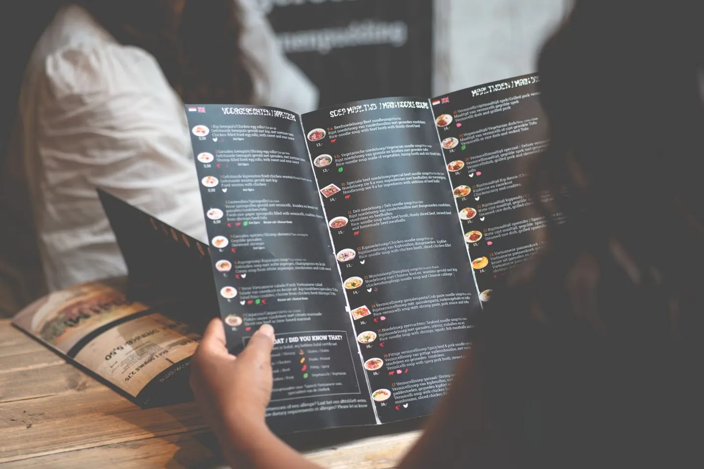 A woman reading a restaurant menu at a wooden table