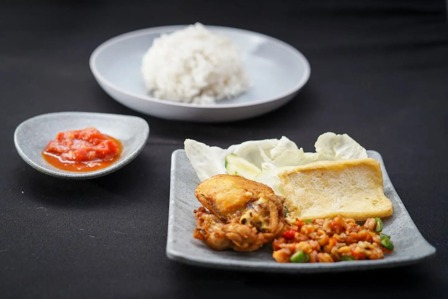 Nasi dengan tahu, ayam goreng, dan sambal di atas piring