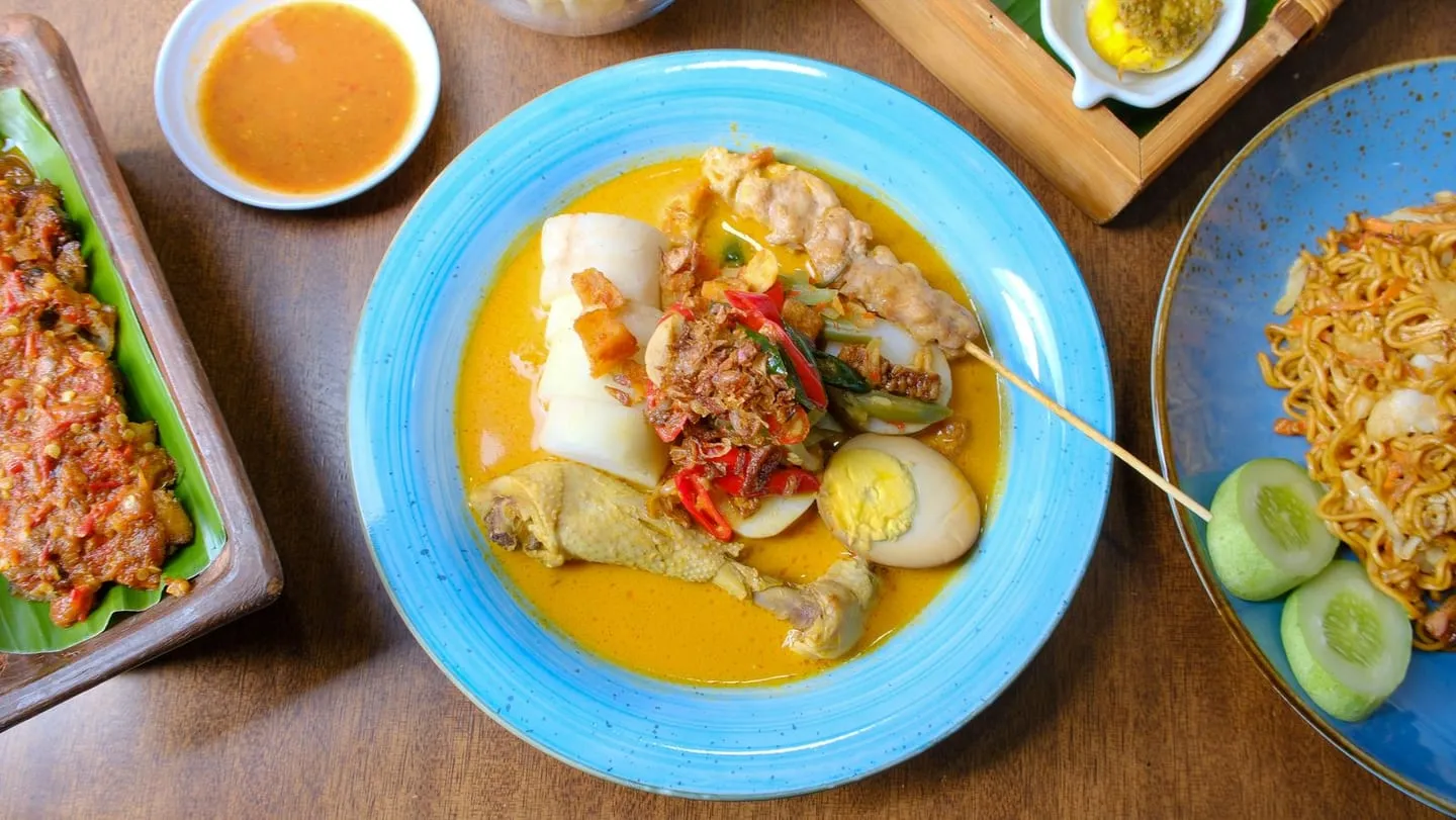 Lontong sayur dengan ayam, telur, dan sate di atas piring biru
