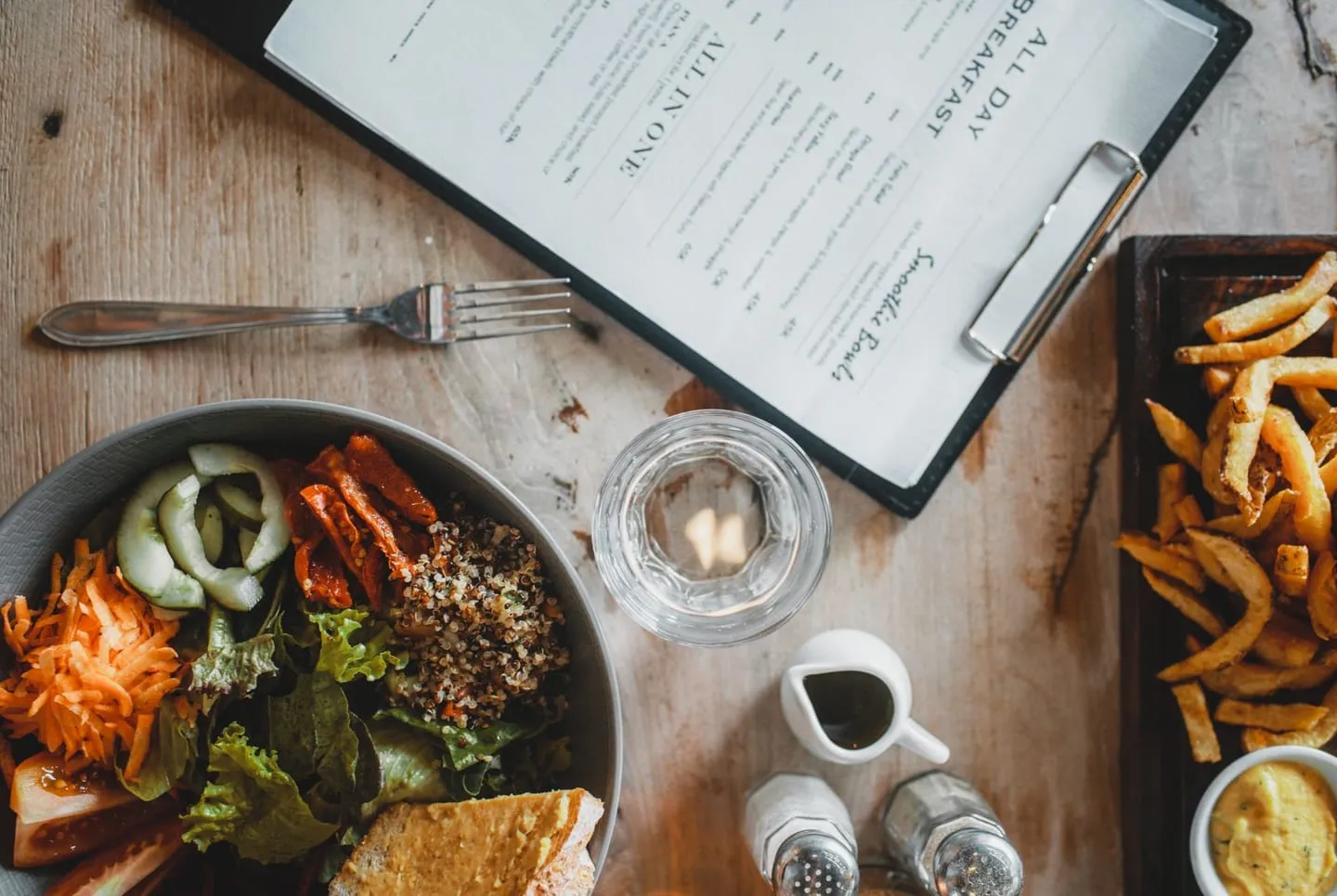 A salad and fries served at a cafe table beside a menu